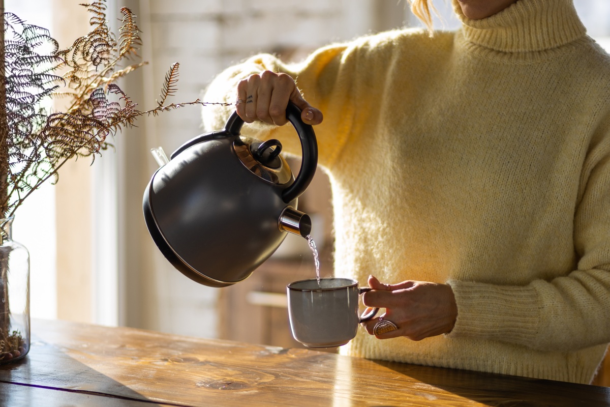 Eine Frau schenkt sich heißes Wasser in eine Tasse.