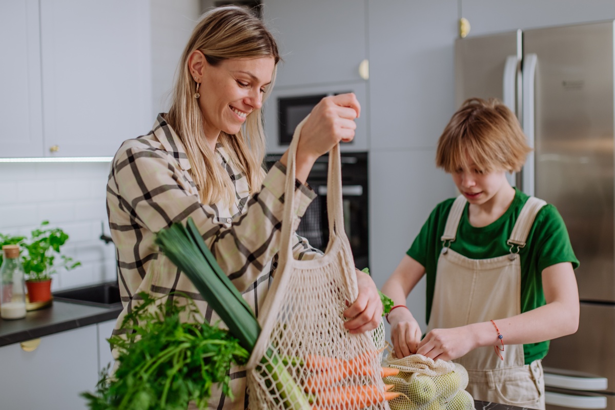 Mutter und Sohn packen Obst und Gemüse das sie eingekauft haben in der Küche aus.